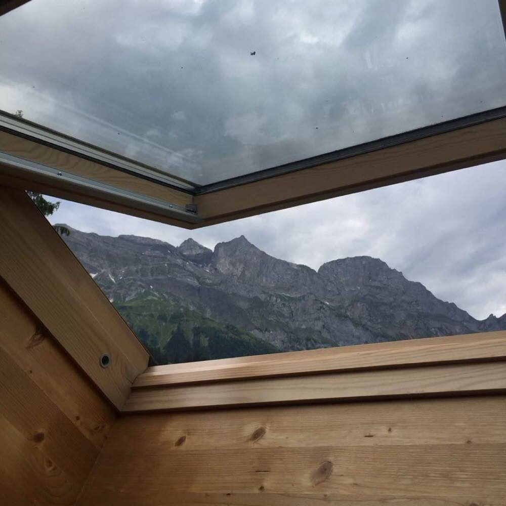 Rocky alpine peaks seen through an open wooden chalet skylight