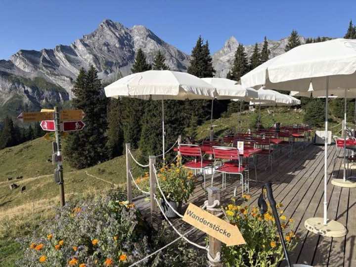 Sunny terrace of a mountain restaurant with red chairs below rugged Alps