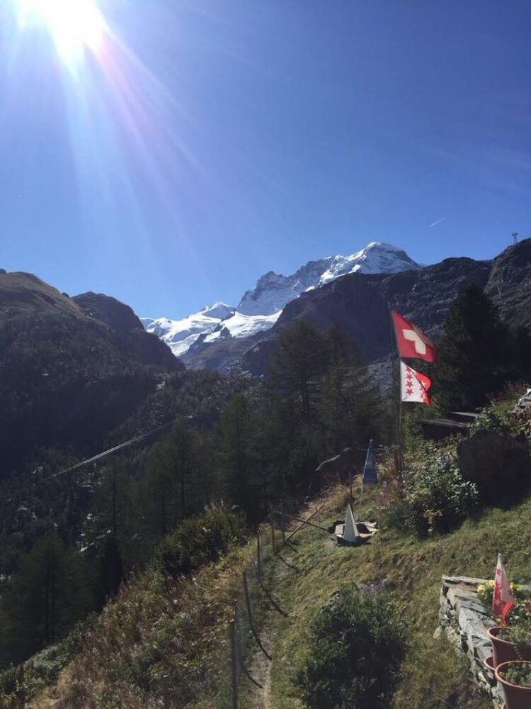 Sunlit alpine trail with Swiss flags above the Saas valley