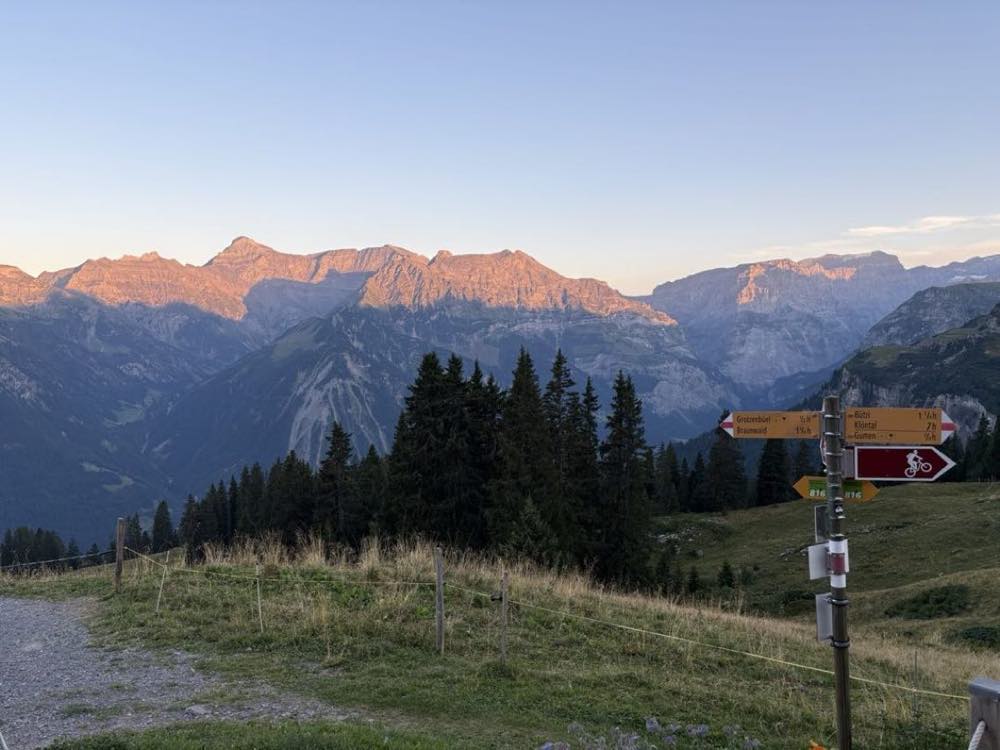 Alpenglow on the Glarus Alps at dawn beside a Swiss hiking signpost