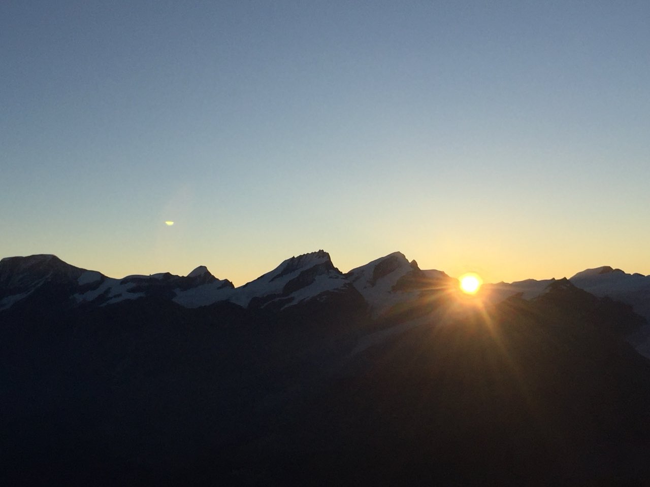Sunrise over silhouetted Swiss Alps with the sun rising between the peaks